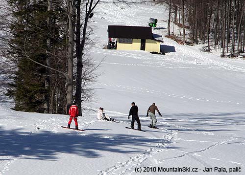 Three guys and one girl are trying some snowboarding in the lower part of ski resort near two-chair lift