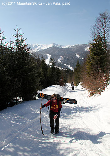 Jana si nese snowboard napříč a opírá se o čerstvě ulomenou větev